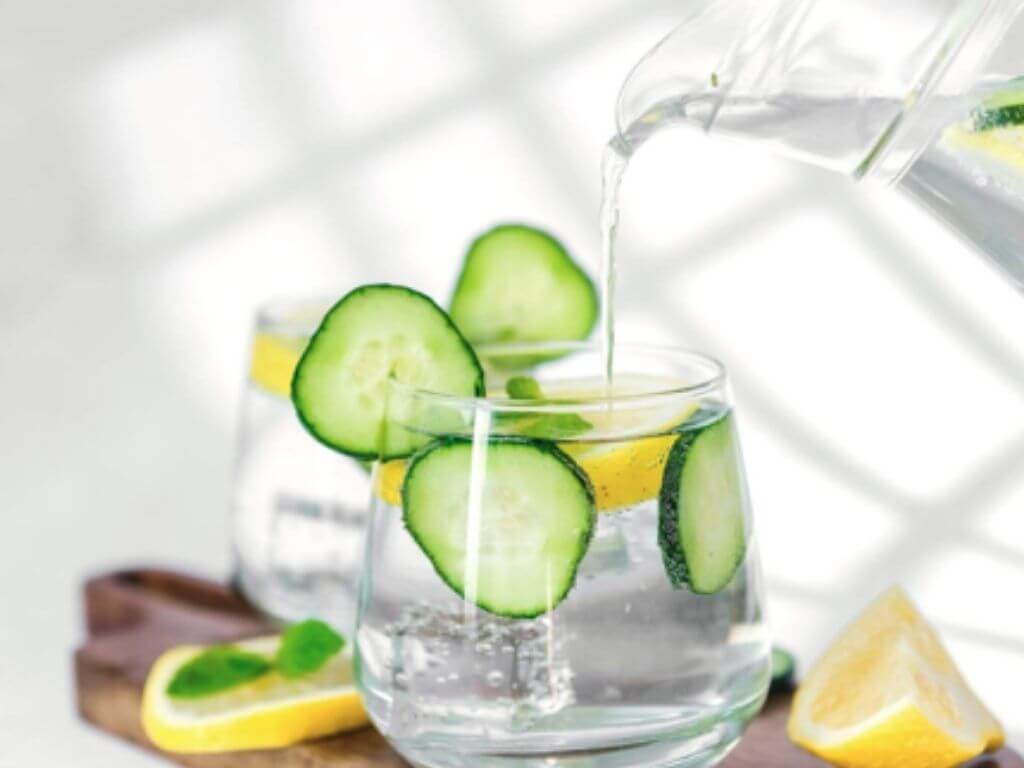 Water in jar poured into a glass with fresh cucumber, mint and lemon slices.