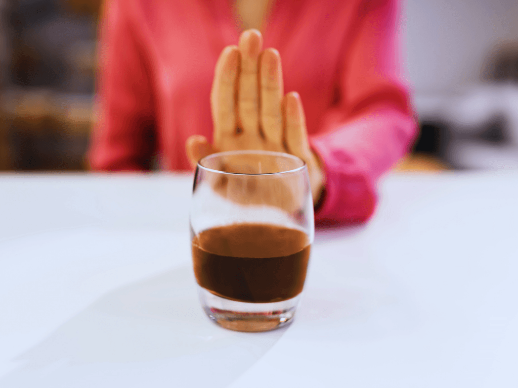 Hand pushing a glass of brown wisky/ alcohol away as a gesture of protecting liver health.