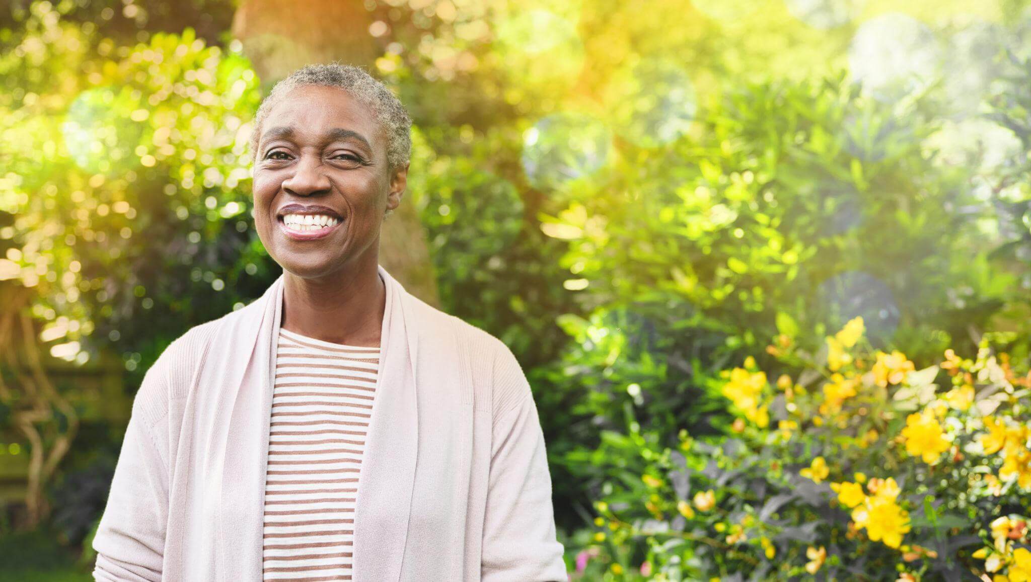 Healthy mature black woman smiling in a natural environment with trees and bright sun light.